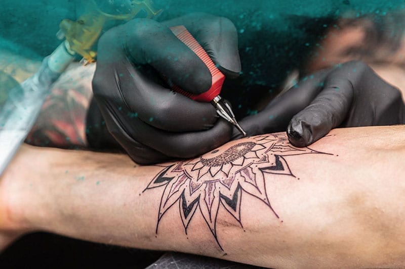 Tattoo artist working on flower arm tattoo