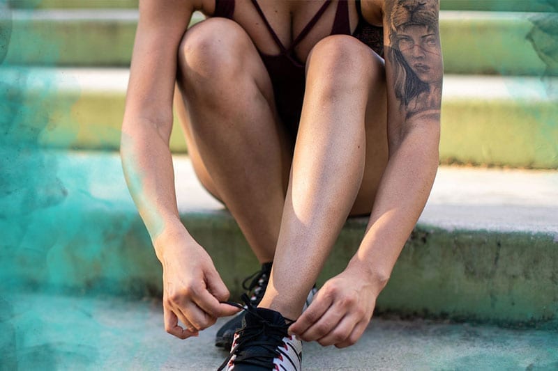 woman with arm tattoo tying running shoes