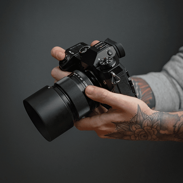 close up of a pair of tattooed hands holding a professional camera