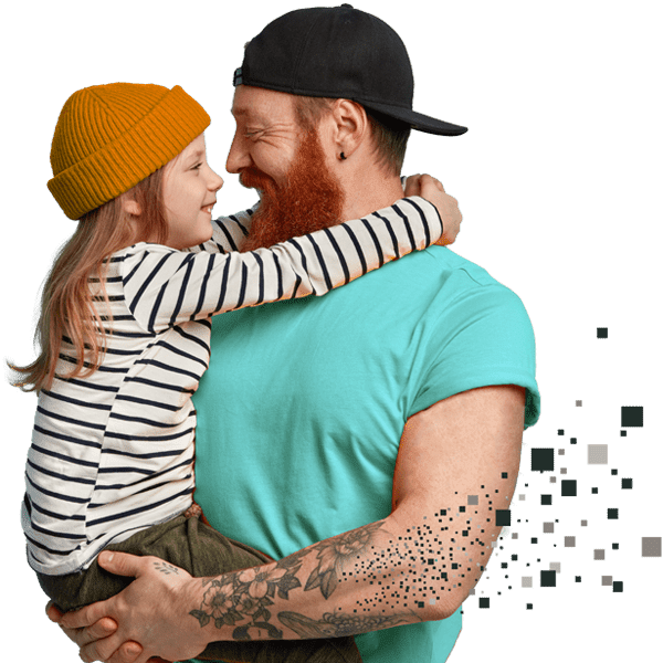 A dad with a red beard is wearing a teal shirt and black hat. He is holding his daughter who is wearing an orange beanie and a black and white long sleeved shirt