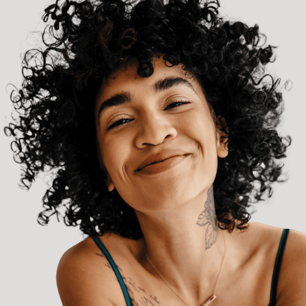 A woman with a curly afro and a neck tattoo smiles at the viewer