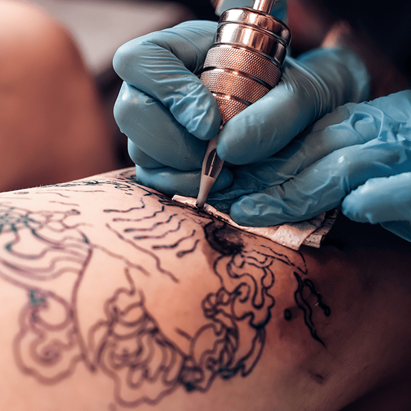 close up of the gloved hands of a tattoo artist while they give someone a black line art tattoo